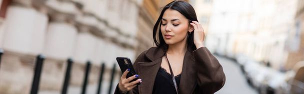 młoda brunetka kobieta patrząc na telefon komórkowy na rozmytej ulicy w Pradze, baner - Zdjęcie, obraz