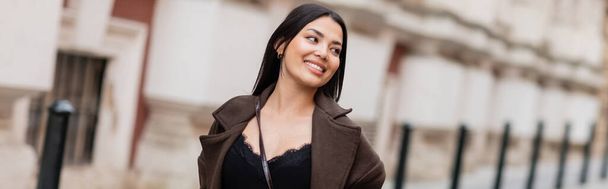vidám barna nő kabátban mosolyog a város utcáin Prágában, banner - Fotó, kép