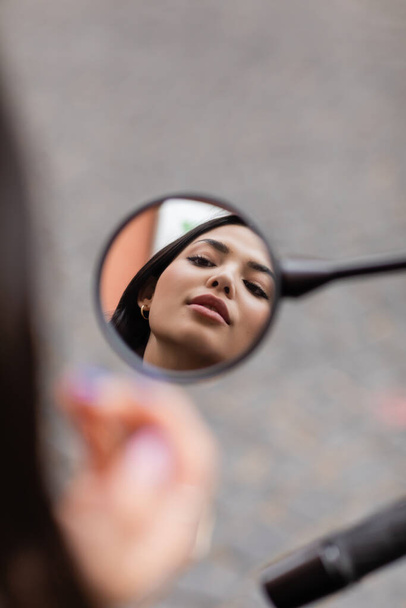 young brunette woman with makeup looking in mirror on blurred foreground - Foto, Bild