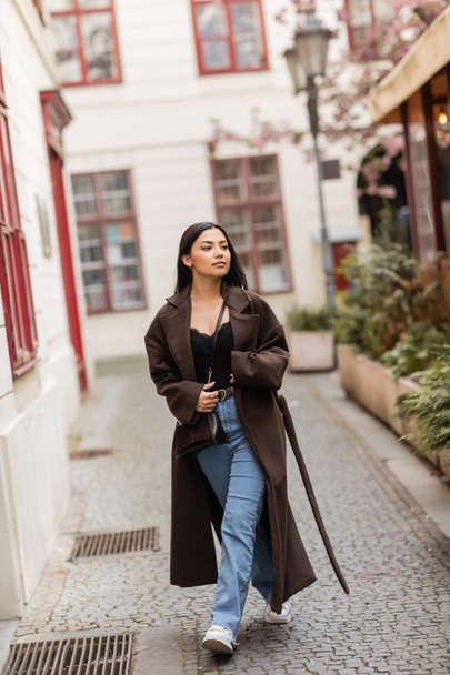 full length of young woman in trendy autumn clothes walking along narrow street in prague - 写真・画像