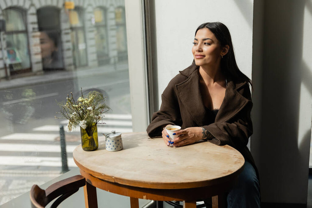 femme heureuse regardant la rue urbaine tout en étant assis près de la fenêtre dans un café à prague - Photo, image