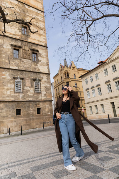 Elegante giovane donna in cappotto e occhiali da sole a piedi sulla strada urbana a Praga  - Foto, immagini