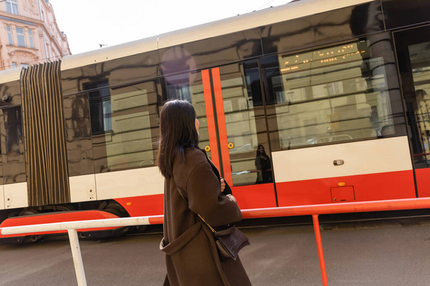 Jeune femme brune en manteau regardant le tram dans la rue à Prague  - Photo, image