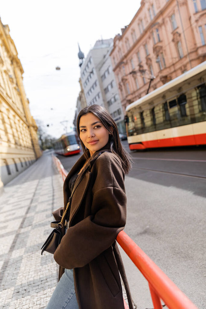 Улыбающаяся женщина в пальто смотрит в камеру на городской улице в Праге  - Фото, изображение