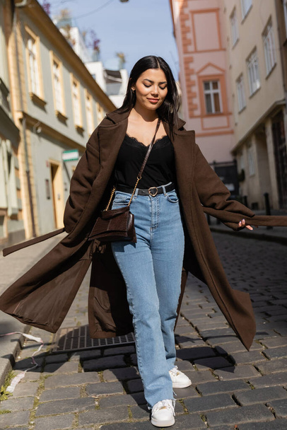 Smiling woman in coat walking on road on urban street in Prague  - Fotoğraf, Görsel