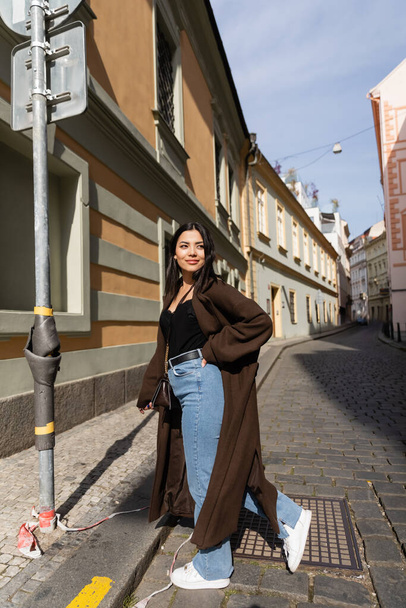 Stylish tourist in coat walking on road near buildings in Prague  - Фото, изображение