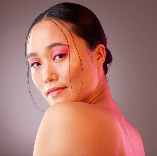 Face, eyeshadow and neon makeup of woman on gray studio background. Portrait, unique skincare or facial beauty cosmetics treatment of a beautiful female, girl or model from Japan with glowing skin - Photo, Image