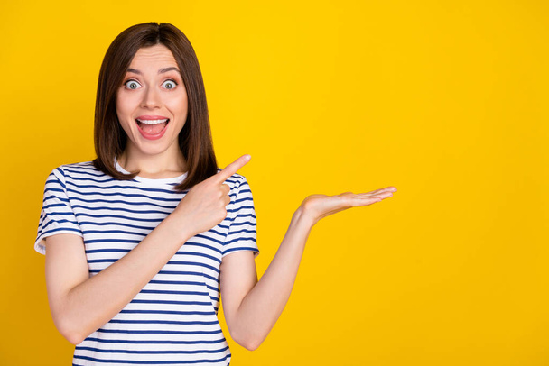 Portrait photo of young attractive woman crazy shocked holding product directing finger unexpected how cool this isolated on yellow color background. - 写真・画像
