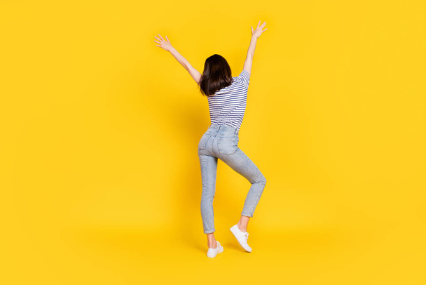 Rear back behind view portrait of pretty lady wear fashionable jeans striped t shirt raise arm isolated on yellow color background. - Photo, image
