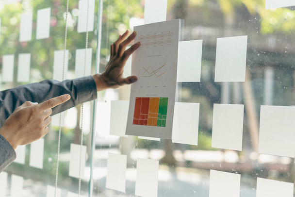 Business Crisis Concept : Hands pointing to a financial business graph to analyze the problem. Business team working in marketing on statistics, reports, graphs, financial documents on glass wall. - Photo, Image