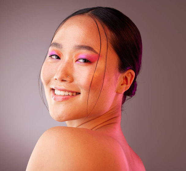 Beauty, makeup and face of model in studio with neon, creative and color vaporwave, eyeshadow and mockup. Portrait, art and Chinese model smile, happy and relax with facial cosmetics grey background. - Photo, image