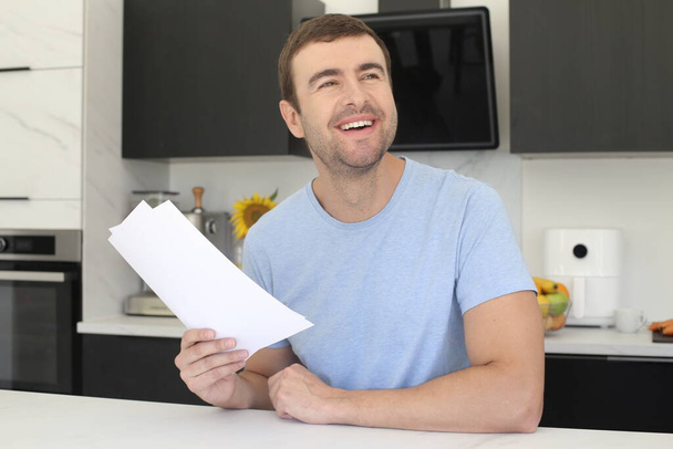 portret przystojnego młodego mężczyzny trzymającego papier ze zszokowanym wyrazem twarzy w kuchni - Zdjęcie, obraz