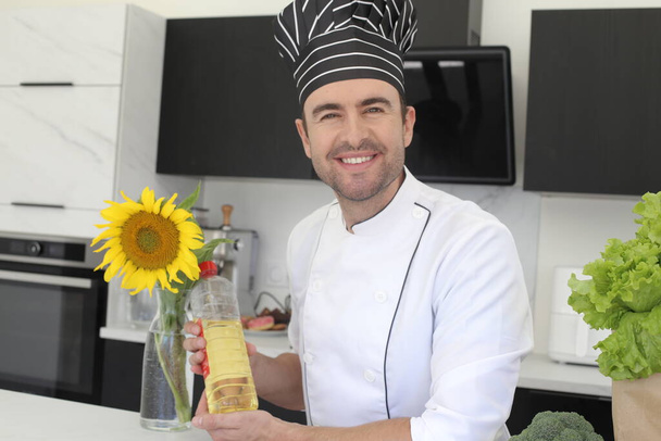 portrét pohledného mladého kuchaře s lahví slunečnicového oleje v kuchyni - Fotografie, Obrázek