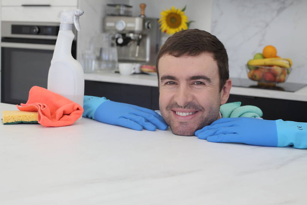 портрет красивого молодого человека с чистящим спреем и принадлежностями на кухне - Фото, изображение
