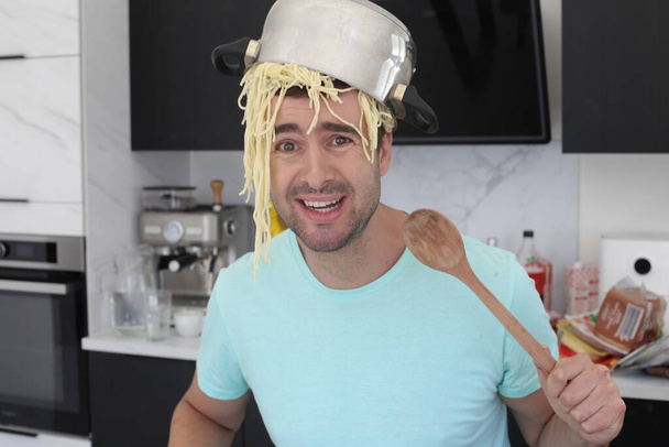 portret przystojnego młodzieńca z garnkiem spaghetti na głowie w kuchni - Zdjęcie, obraz