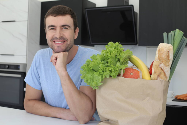 portret van knappe jongeman met zak verse groenten in de keuken - Foto, afbeelding