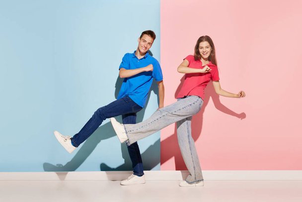 Portrait of young couple, man and woman in casual clothes dancing isolated over blue-pink background. Happy. Concept of youth culture, fashion, relationship, emotions. Copy space for ad - Foto, Imagem