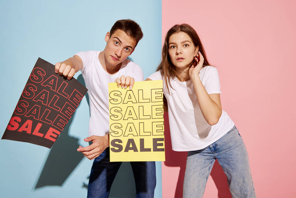 Portrait of young people, man and woman in casual clothes holding paper with big sales information. Holiday shopping . Concept of youth culture, fashion, relationship, emotions. Copy space for ad - Φωτογραφία, εικόνα