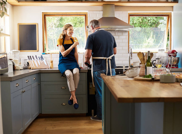 Couple, wine and cooking in kitchen, happy and talking while bonding, conversation and home. Senior, man and woman in retirement with glass, food and together in house with love, romance and laugh. - Photo, Image