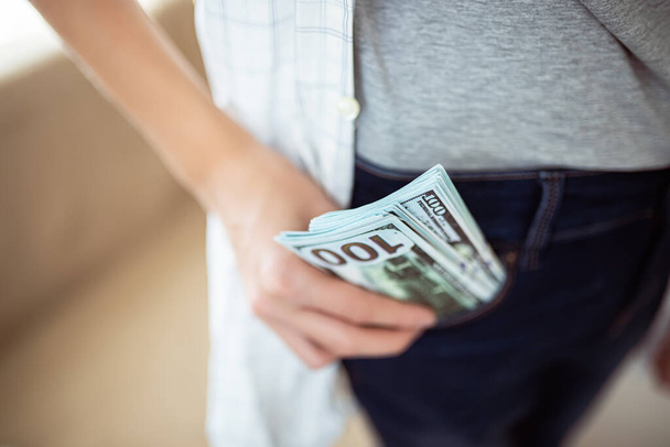 A tinédzser egy köteg dollárt tesz a zsebébe. Készpénzfizetés - Fotó, kép