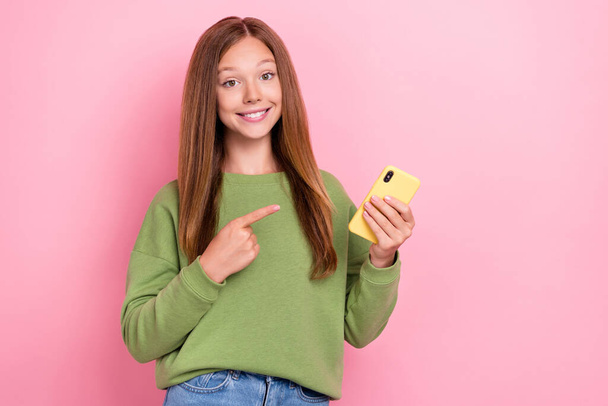 Portrait of positive good mood girl long hairstyle dressed green sweatshirt directing at smartphone isolated on pink color background. - Fotoğraf, Görsel