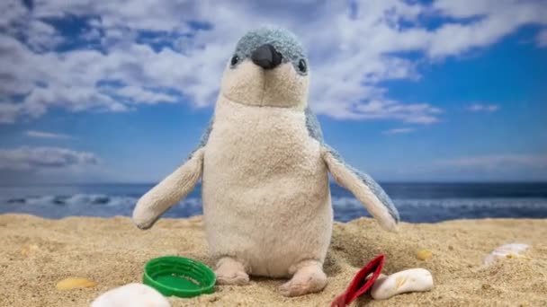 A penguin teddy surrounded by rubbish and trash filling up on a beautiful beach  - Footage, Video