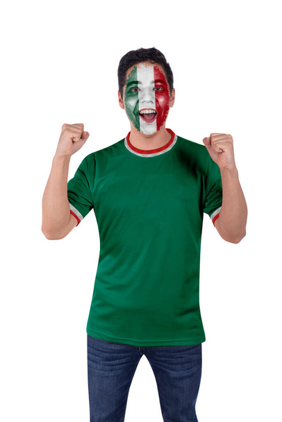 Молодий спортивний і футбольний фанатик з зеленою мексиканською майкою радісно кричить з хвилюванням за перемогу своєї улюбленої команди.. - Фото, зображення