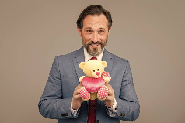 happy man with occasion greeting. businessman show toy and heart. valentines day. be my valentine. present for womens day. senior ceo hold toy bear. grizzled man prepare for love date. - Fotó, kép