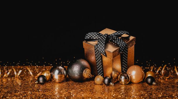 Felicidades Feliz Navidad y Feliz Año Nuevo. Caja dorada con un regalo y bolas de Navidad sobre fondo negro y dorado - Foto, Imagen