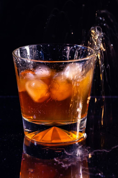 A vertical shot of ice splashing into a glass of whiskey on a black background - Foto, Bild