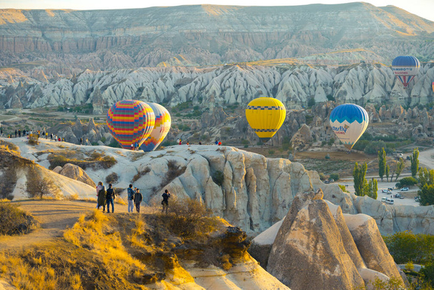 昼間にカッパドキアの山の風景の上を飛ぶ熱気球を見て丘の上の観光客。水平射撃だ。高品質の写真 - 写真・画像
