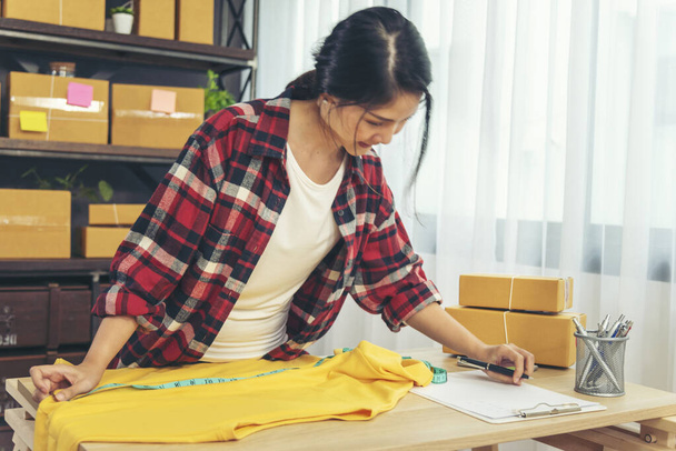 Módní návrhářka Ženy měří oblečení design balení box na stole. Ženy kontrolují velikost zboží, kvalitu balení do krabice. Podnikatel asijské žena startup malý obchod na domácí kanceláři stolu - Fotografie, Obrázek