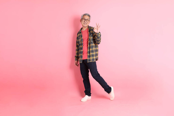 The full length of senior Asian man standing on the pink background. - Foto, afbeelding