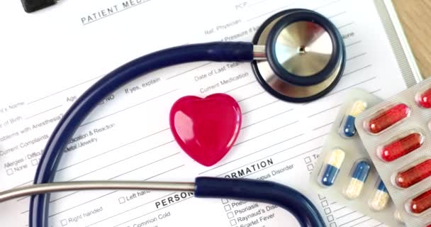 Rode speelgoed hart ligt op medische documenten met stethoscoop en pillen close-up 4k film slow motion. Cardiologie - concept van medische zorg - Video