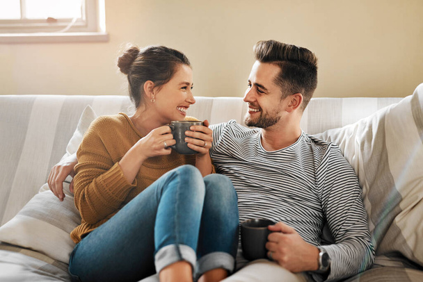 Creo que estás más caliente que mi café. una joven pareja relajándose en el sofá en casa - Foto, Imagen