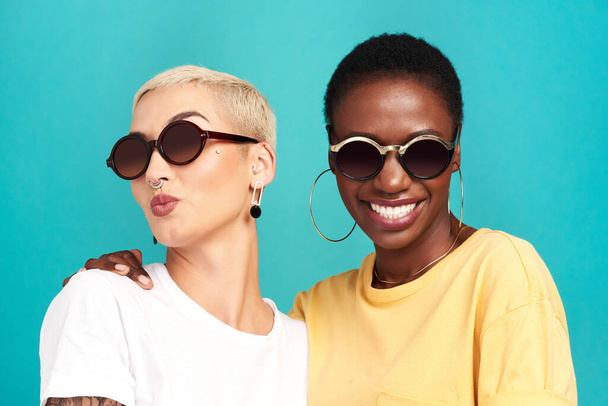 友人を選ぶようにあなたの様式を選びなさい。ターコイズを背景にサングラスをかけた2人の若い女性のスタジオショット - 写真・画像