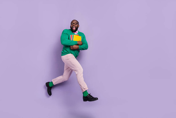 Full body image of excited young teacher running to his classroom hold class materials isolated on violet color background. - Foto, Imagem