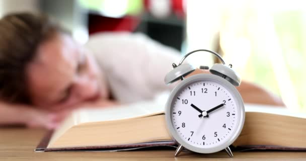 Reloj despertador de pie cerca de la mujer durmiendo en primer plano libro 4k película cámara lenta. Concepto de fecha límite - Metraje, vídeo