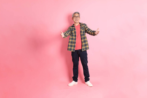 The full length of senior Asian man standing on the pink background. - Photo, image