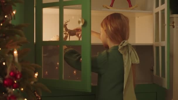 Αξιολάτρευτο κορίτσι που κρατάει παιχνίδια ταράνδων και παίζει στο σπίτι την παραμονή των Χριστουγέννων, κοντά στο χριστουγεννιάτικο δέντρο στο σπίτι. Χαρούμενη διάθεση. Αργή κίνηση. Υψηλής ποιότητας 4k πλάνα - Πλάνα, βίντεο