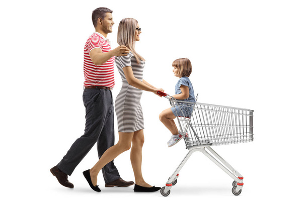 Full length profile shot of a couple pushing a shopping cart with their child seated isolated on white background - 写真・画像