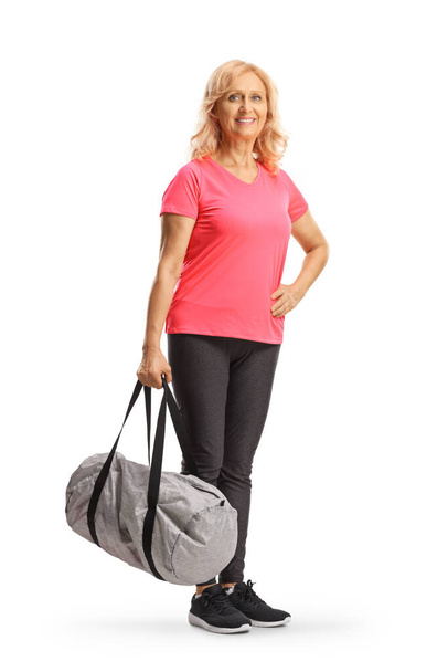Smiling mature woman in sportswear holding a sports bag isolated on white background - Фото, зображення