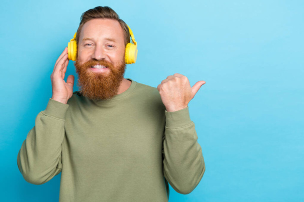 Photo of cheerful positive guy dressed khaki long sleeve directing empty space hand touch headphones isolated on teal color background. - Фото, изображение
