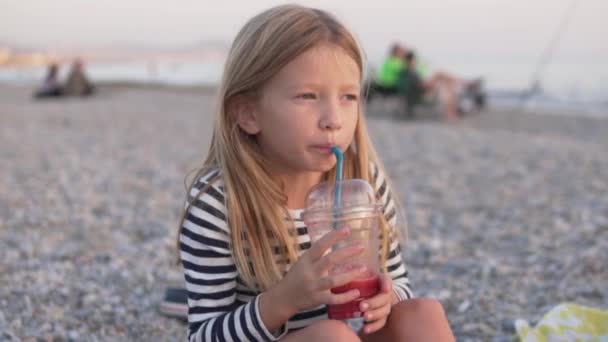 Uma menina engraçada bebe suco de romã de um copo de plástico no mar. As crianças de conceito crescem no mar. Viajar com crianças. Turquia, Alanya, outubro - Filmagem, Vídeo