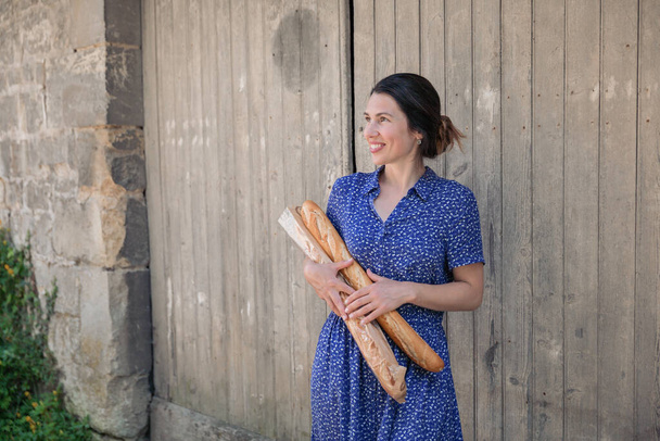 Young pretty woman standing with french baguettes in her hands in the countryside - Foto, Bild