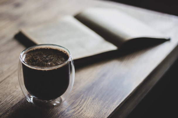 Cup of coffee and opened book. Coffee cup and ancient book on wooden table. Literature concept. Autumn still life. Espresso in library. Knowledge and wisdom. Cozy interior. Glass of coffee and book. - Photo, Image
