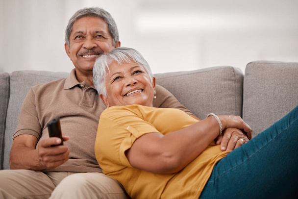 Happy senior couple, love and watching tv relax together on living room sofa at family home. Elderly married man and woman, chill and watch television on couch bonding, laughing and smile at movie. - Foto, imagen