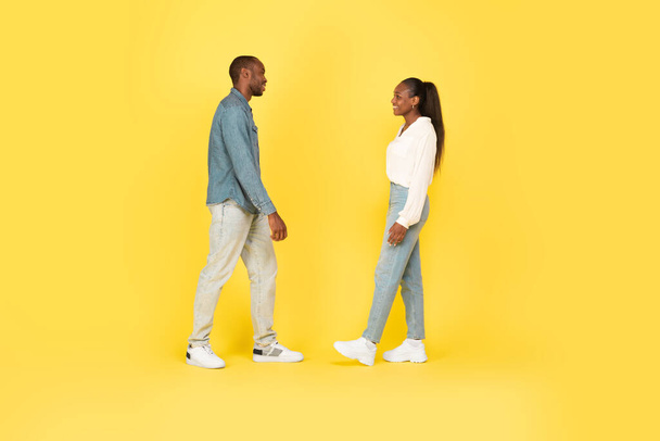 Ευτυχισμένος Αφρο-Αμερικανός άντρας και γυναίκα περπατώντας συναντιούνται πάνω από κίτρινο φόντο στούντιο. Χιλιετίες ζευγάρι ποζάρουν μαζί. Πλήρες μήκος, πλευρική άποψη shot - Φωτογραφία, εικόνα