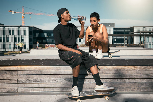 Skateboard, drinking water and friends with a black man and woman skater outdoor in a city for fun or recreation together. Couple, skating and summer with a male and female in an urban town to skate. - Fotoğraf, Görsel