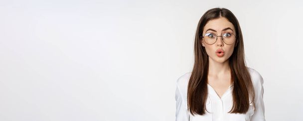 Primer plano retrato de mujer corporativa en gafas, mirando sorprendida, asombrada e intrigada, de pie sobre fondo blanco. - Foto, Imagen